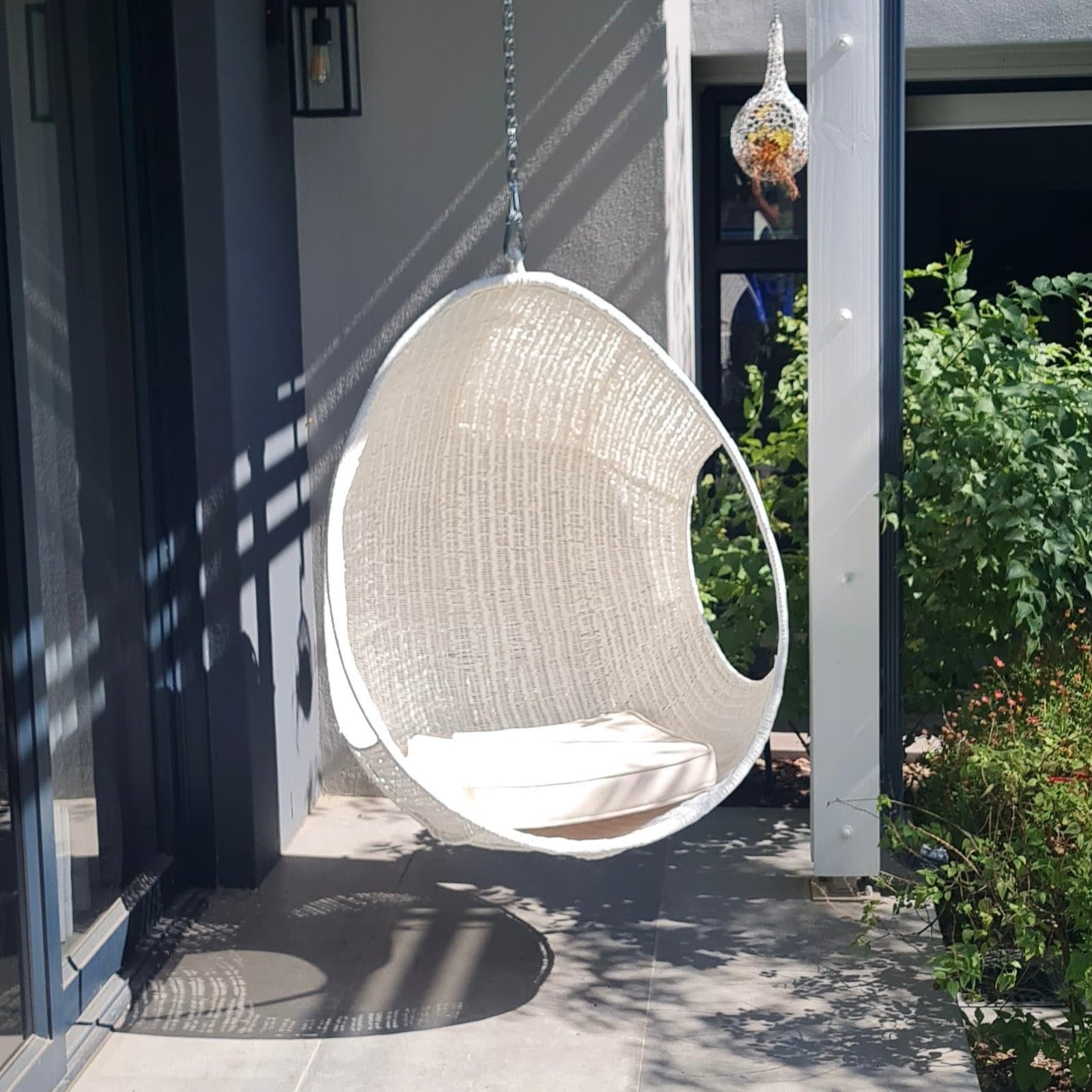 Hand-woven Malawi cane Hanging POD Chair with egg-shaped, cocoon-like structure suspended by sturdy rope, shown in natural finish. The chair features an open weave and rounded form designed as a personal relaxing sanctuary, with customizable detachable cushions (natural, white, or black) for added comfort.
