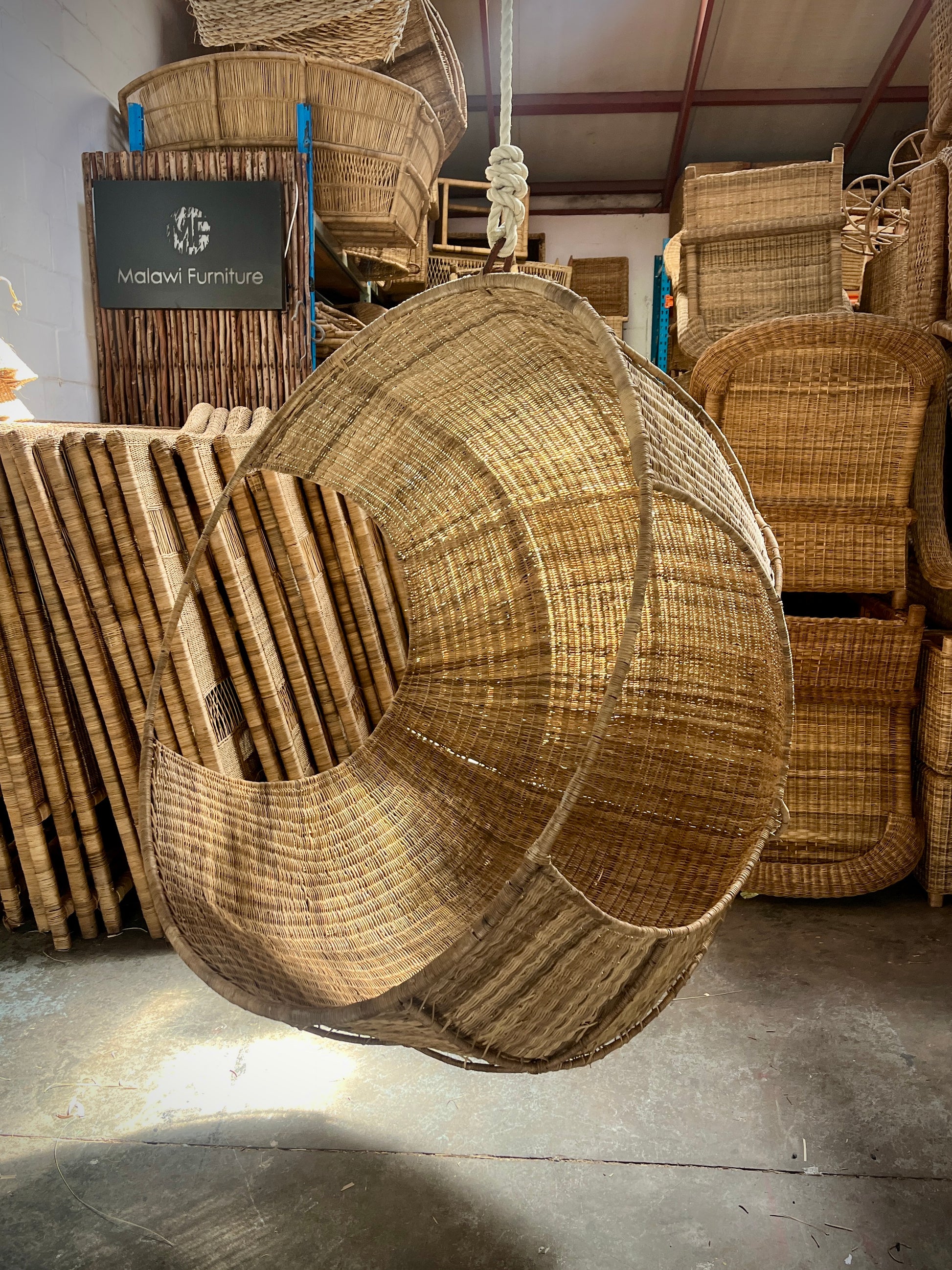 Hand-woven Malawi cane Hanging POD Chair with egg-shaped, cocoon-like structure suspended by sturdy rope, shown in natural finish. The chair features an open weave and rounded form designed as a personal relaxing sanctuary, with customizable detachable cushions (natural, white, or black) for added comfort.