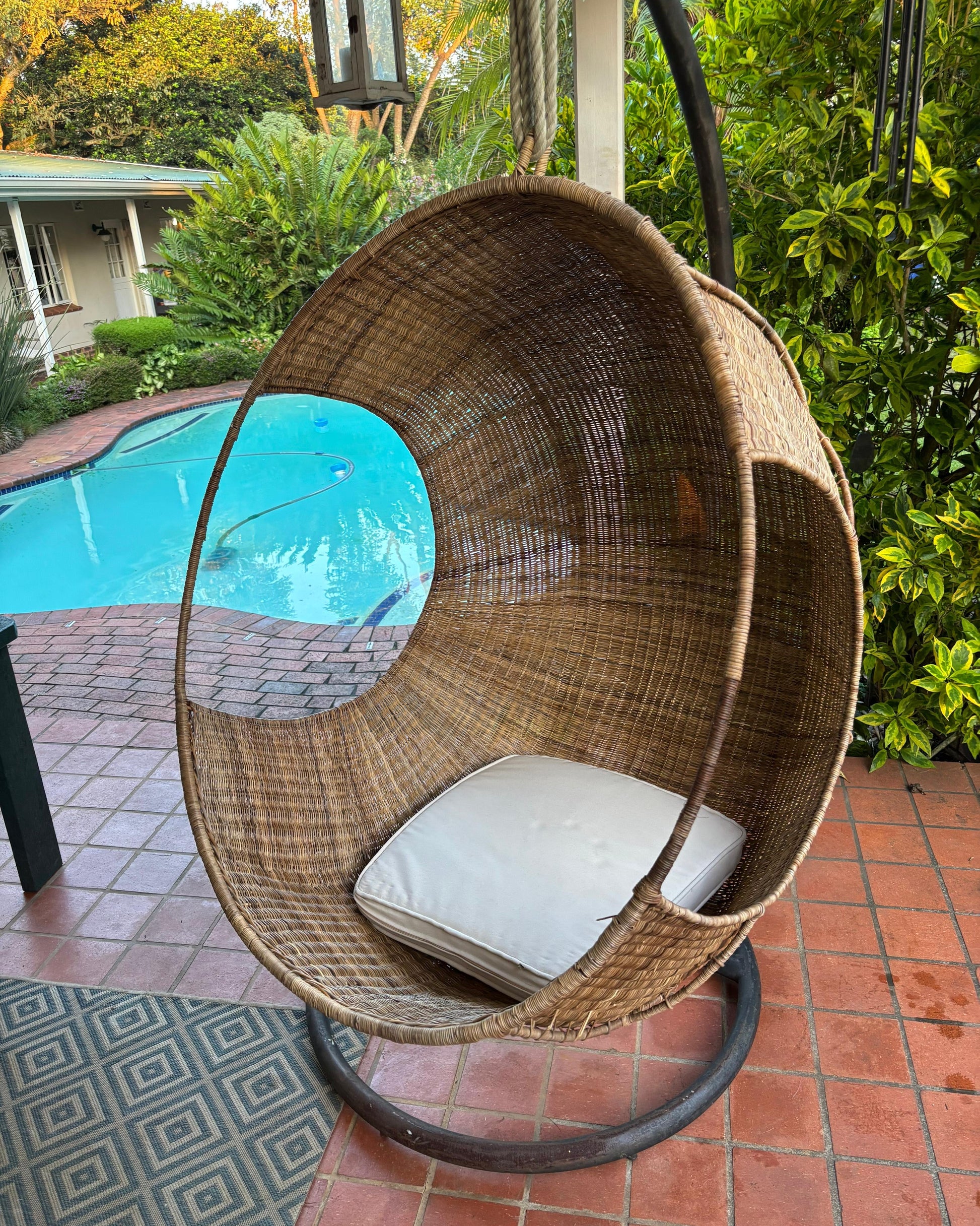 Hand-woven Malawi cane Hanging POD Chair with egg-shaped, cocoon-like structure suspended by sturdy rope, shown in natural finish. The chair features an open weave and rounded form designed as a personal relaxing sanctuary, with customizable detachable cushions (natural, white, or black) for added comfort.