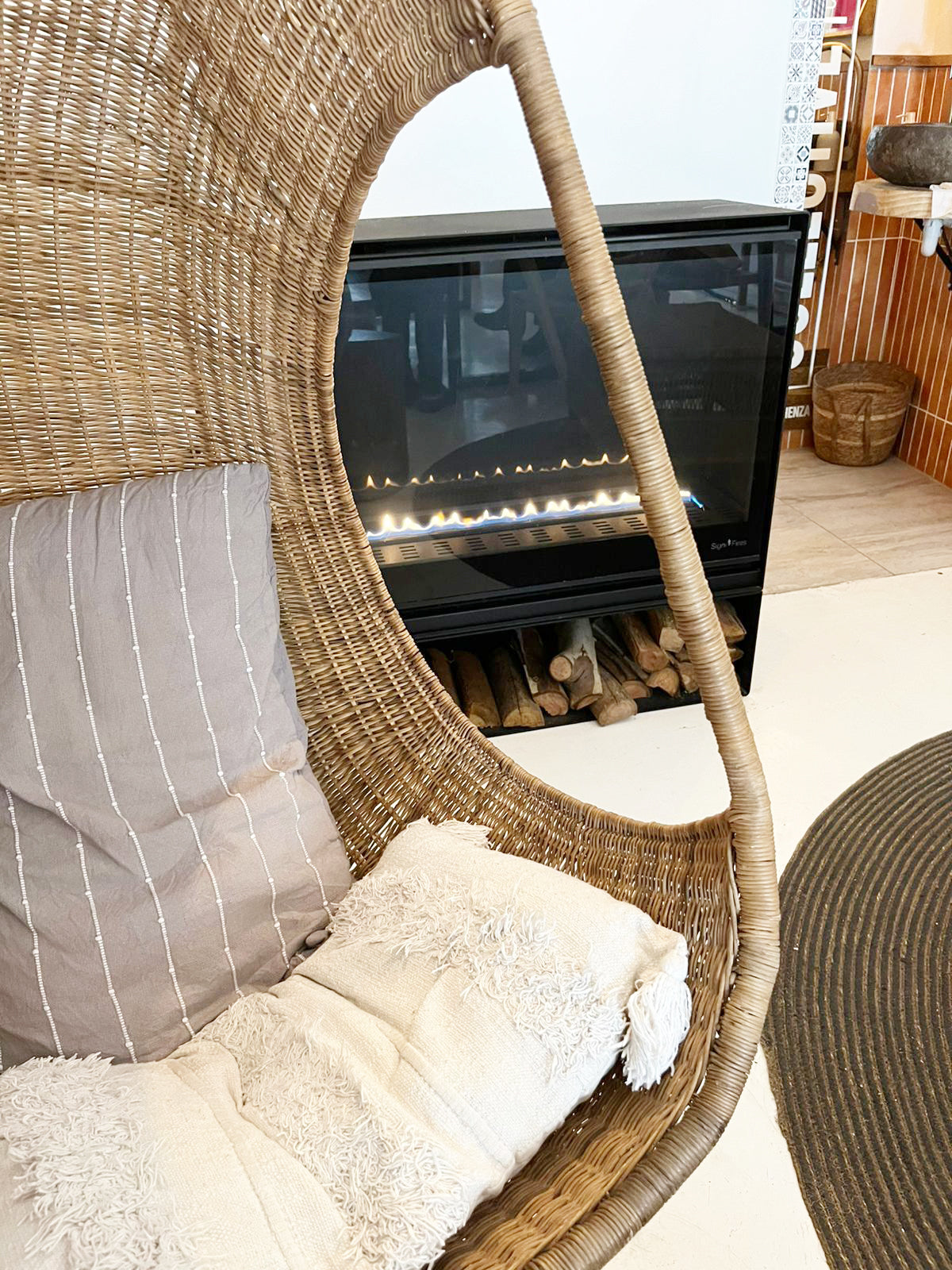 Hanging Egg Chair — A hand-woven, egg-shaped hanging chair crafted from natural Malawi cane. It features a spacious, cocoon-like form and is suspended by a looped rope above. The chair is shown with a soft, plush cushion inside, blending rustic artisanal texture with cozy modern comfort.