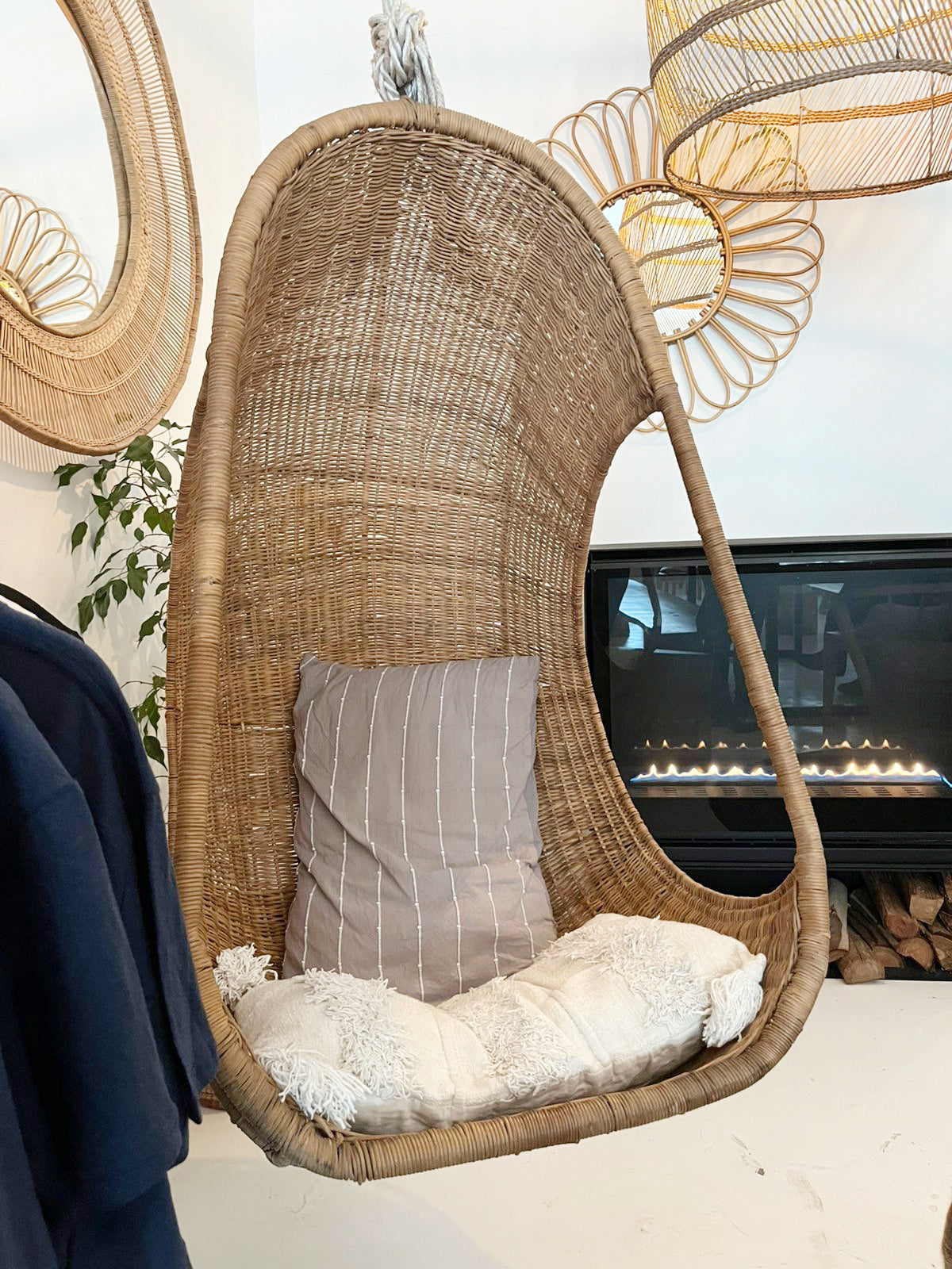 Hanging Egg Chair — A hand-woven, egg-shaped hanging chair crafted from natural Malawi cane. It features a spacious, cocoon-like form and is suspended by a looped rope above. The chair is shown with a soft, plush cushion inside, blending rustic artisanal texture with cozy modern comfort.