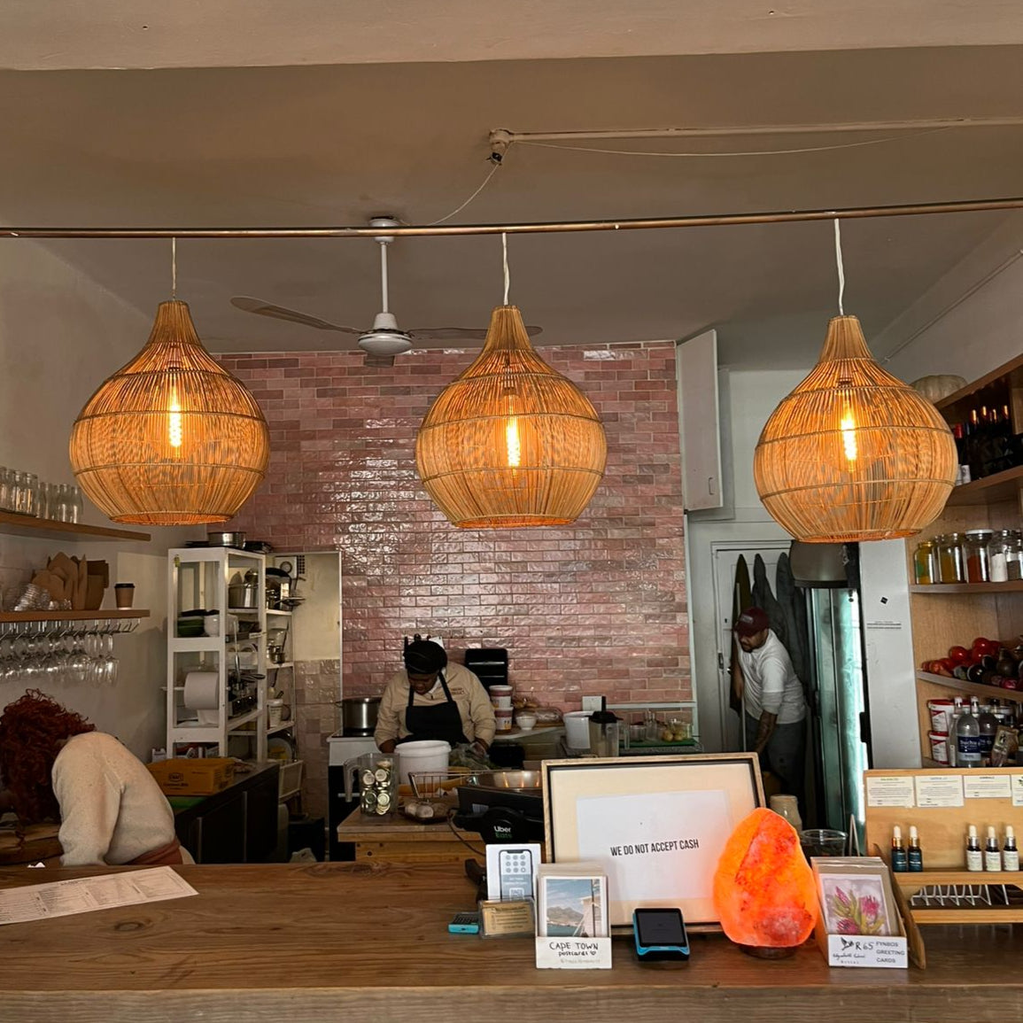 Interior of a cafe with wicker pendant lights, brick wall, and customers at the counter.