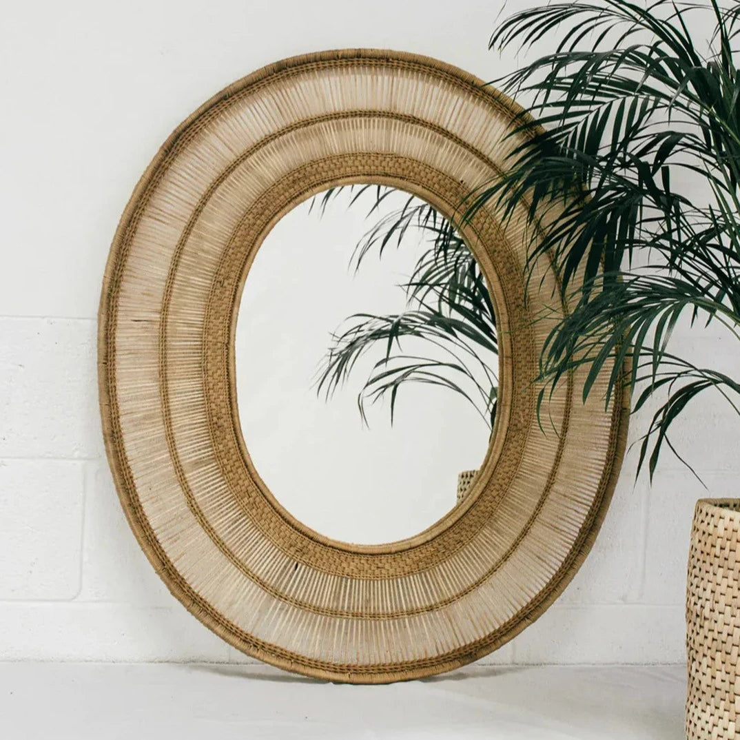 hand-woven cane and bamboo mirror. Crafted by skilled artisans, this exquisite oval piece is perfect for adding a touch of rural charm to any living space. Use it as a unique focal point or mix and match it with other decorative items. Please note: The frame is handmade in Malawi and strengthened in the UK for durability. The mirror is securely fastened using backing board and twine.