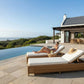 Woman reading a book on a lounge chair by an infinity pool with a scenic view.