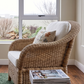 Available Now - Malawi Furniture - Handwoven natural cane Malawi Couch Chair with plush white cushions and a floral pillow in a cozy sunlit corner. Ideal for a relaxed reading nook.