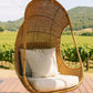 Hanging Egg Chair — A hand-woven, egg-shaped hanging chair crafted from natural Malawi cane. It features a spacious, cocoon-like form and is suspended by a looped rope above. The chair is shown with a soft, plush cushion inside, blending rustic artisanal texture with cozy modern comfort.