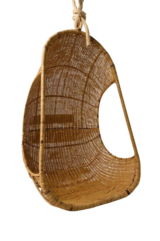 Hanging Egg Chair — A hand-woven, egg-shaped hanging chair crafted from natural Malawi cane. It features a spacious, cocoon-like form and is suspended by a looped rope above. The chair is shown with a soft, plush cushion inside, blending rustic artisanal texture with cozy modern comfort.