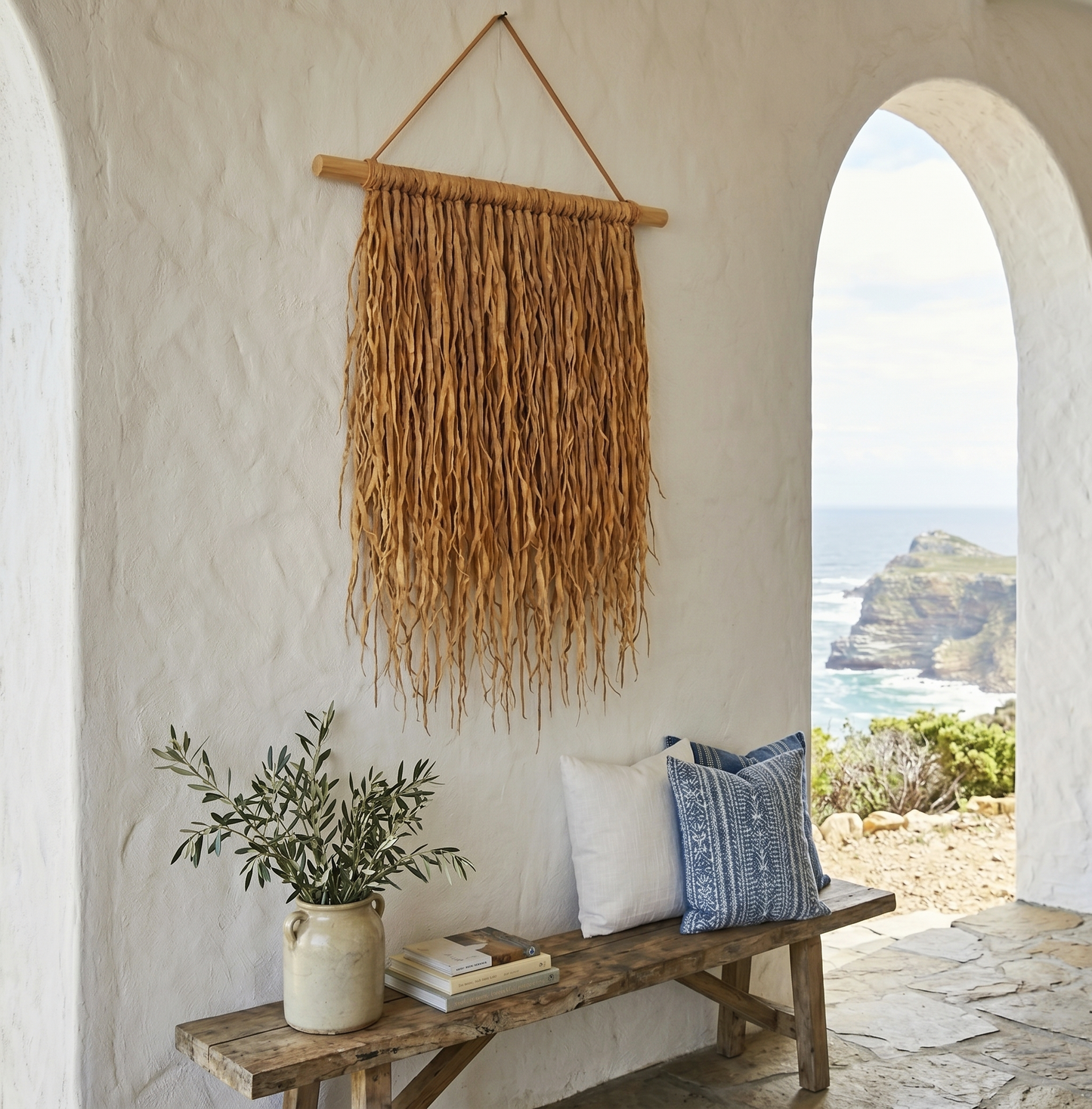 Hanging Grass Wall Decor in a coastal villa. Handcrafted hanging grass wall art by Malawi Furniture, featuring natural dried organic ilala palm and seagrass onto a sustainable wooden dowel. Large 90cm by 1m boho fringed wall hanging in a light natural brown tone for minimalist home decor.