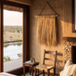 Hanging Grass Wall Decor in an African Safari Lodge. Handcrafted hanging grass wall art by Malawi Furniture, featuring natural dried organic ilala palm and seagrass onto a sustainable wooden dowel. Large 90cm by 1m boho fringed wall hanging in a light natural brown tone for minimalist home decor.