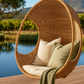 Hand-woven Malawi cane Hanging POD Chair with egg-shaped, cocoon-like structure suspended by sturdy rope, shown in natural finish. The chair features an open weave and rounded form designed as a personal relaxing sanctuary, with customizable detachable cushions (natural, white, or black) for added comfort.