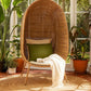 Standing EGG Chair — A handcrafted, egg-shaped chair woven from natural Malawian cane, featuring an elegant cocoon silhouette that rests on a sleek, four-legged metal stand. The chair includes a removable plush cushion (available in natural, white, or black) that enhances comfort and style. This artisanal piece combines organic textures with modern minimalism, making it a striking focal point for both indoor and outdoor spaces.