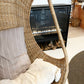 Hanging Egg Chair — A hand-woven, egg-shaped hanging chair crafted from natural Malawi cane. It features a spacious, cocoon-like form and is suspended by a looped rope above. The chair is shown with a soft, plush cushion inside, blending rustic artisanal texture with cozy modern comfort.