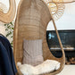 Hanging Egg Chair — A hand-woven, egg-shaped hanging chair crafted from natural Malawi cane. It features a spacious, cocoon-like form and is suspended by a looped rope above. The chair is shown with a soft, plush cushion inside, blending rustic artisanal texture with cozy modern comfort.