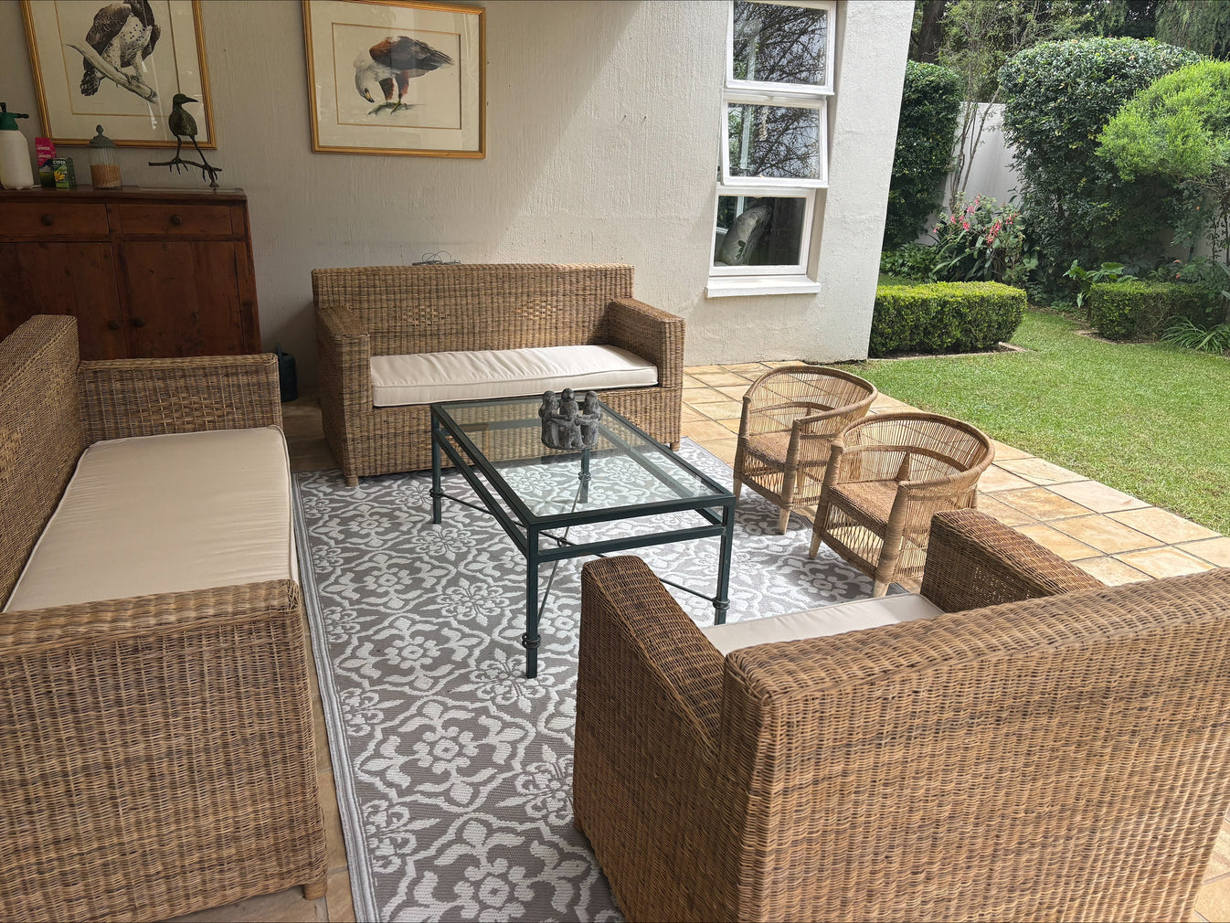 Outdoor patio with wicker furniture and a glass coffee table on a patterned rug.