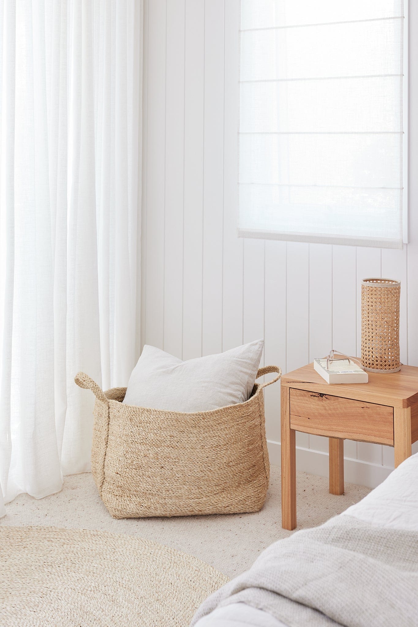 Woven basket with pillows on a bed in a softly lit bedroom.